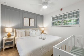 Ein Schlafzimmer mit Bett, Nachttischen, einem Fenster mit Jalousien und einem Deckenventilator.