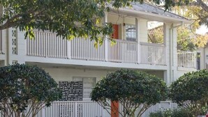 Ein zweistöckiges Gebäude mit weißer Fassade, einem Balkon im oberen Stockwerk und einem verschlossenen Eingang.