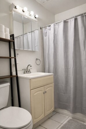 A bathroom with a toilet, sink, vanity, and a shower curtain.