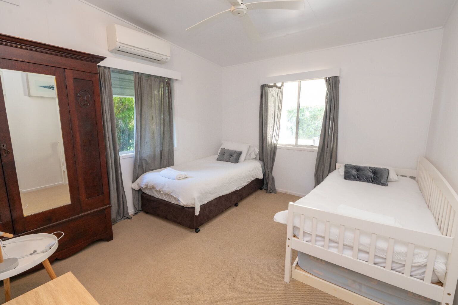 A bedroom with a large bed, a smaller bed, a crib, a wardrobe, and a window with curtains.