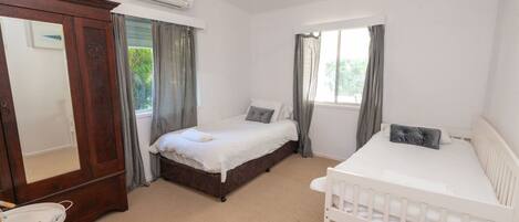 A bedroom with a large bed, a smaller bed, a crib, a wardrobe, and a window with curtains.