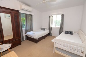 A bedroom with a large bed, a smaller bed, a crib, a wardrobe, and a window with curtains. - A Little Grey Shack - Beach Cottage Amity Point (Amity Point)