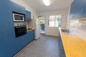 A compact kitchen with blue cabinets, a microwave, stove, and a refrigerator. - A Little Grey Shack - Beach Cottage Amity Point (Amity Point)