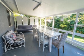 A covered patio with a dining table and chairs, a sofa, and a wicker chair. - A Little Grey Shack - Beach Cottage Amity Point (Amity Point)