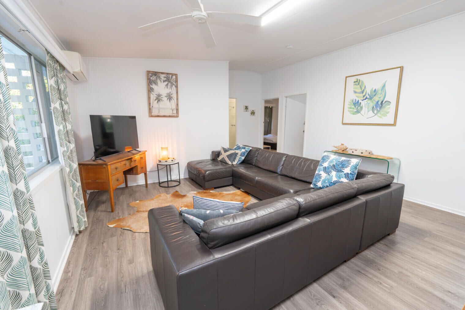 Een moderne woonkamer met een leren bank, een houten bureau, een televisie en kunstwerken aan de muur.