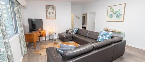 Een moderne woonkamer met een leren bank, een houten bureau, een televisie en kunstwerken aan de muur.