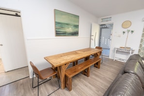 A dining area with a wooden table and benches, a sofa, and a painting on the wall. - A Little Grey Shack - Beach Cottage Amity Point (Amity Point)