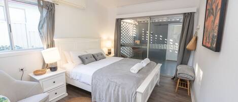 A modern bedroom with a bed, bedside table, lamp, chair, and a view of the outside.