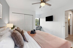 A bedroom with a bed, pillows, a bedside table, a ceiling fan, a TV mounted on the wall, and a door leading to another room. - Red Mountain Shadows Retreat: Sleeps 6 in West Sedona Near Hiking Trails, Park & Bike Paths (Sedona)
