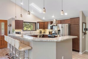 A modern kitchen with a large island, bar stools, stainless steel appliances, and pendant lighting. - Red Mountain Shadows Retreat: Sleeps 6 in West Sedona Near Hiking Trails, Park & Bike Paths (Sedona)