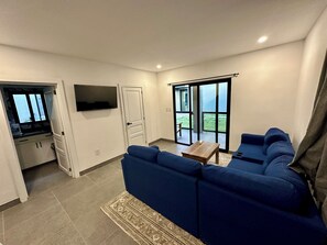 Ein modernes Wohnzimmer mit einem blauen Sofagarnitur, einem kleinen Holztisch und einem an der Wand montierten Fernseher.