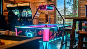 A neon-lit arcade table with a racing game interface, surrounded by wooden walls and a view of the outdoors.