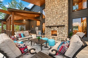 An outdoor living area with a stone fireplace, seating, and a pergola structure.