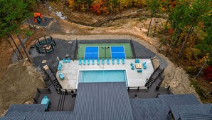 A rooftop with a tennis court, lounge chairs, and a pool.