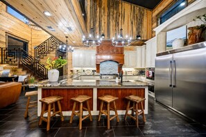 A modern kitchen with a central island, bar stools, stainless steel appliances, and a wooden ceiling.