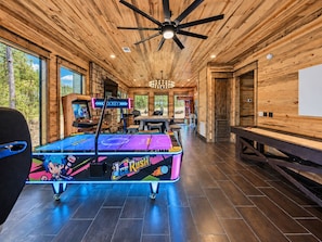 A room with a pool table, arcade games, and a ceiling fan.