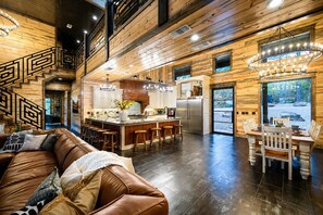 A spacious living area with a brown leather sofa, a dining table with chairs, and a kitchen with a central island. - Heated Pool + Pickleball | Pets | Sauna | Sleep 32 (Broken Bow)