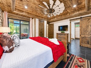 A bedroom with a large bed, wooden ceiling, and a television on the wall.