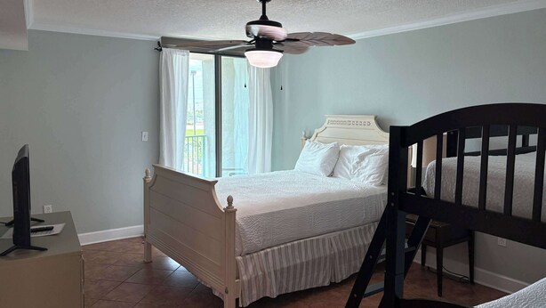 Un dormitorio con cama, ventilador de techo, ventana con cortinas y escritorio con computadora.