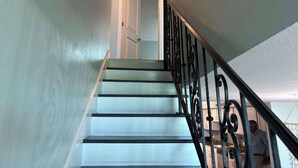 Una escalera con peldaños blancos y barandillas negras que conduce a una puerta.