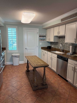 A kitchen with white cabinets, a wooden table, a dishwasher, and a window with blinds. - Perdido Key Paradise Beachfront 3BR (Pensacola)