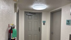 Un pasillo con un extintor fijado a la pared, una puerta con el símbolo de número y una lámpara en el techo.