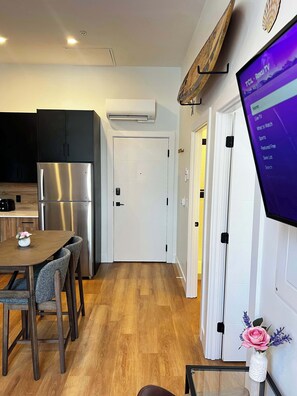 A modern kitchen with a stainless steel refrigerator, a dining table with chairs, and a mounted television displaying a menu. - Sunrise Surf Suite, Downtown Halifax (Halifax)