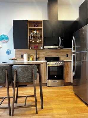 A modern kitchen with a central island, stainless steel appliances, and wooden cabinetry. - Sunrise Surf Suite, Downtown Halifax (Halifax)