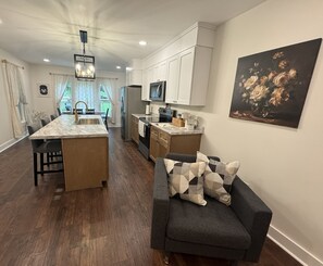 Una cocina moderna con armarios blancos, una isla de mármol y un comedor con mesa y sillas de madera oscura.