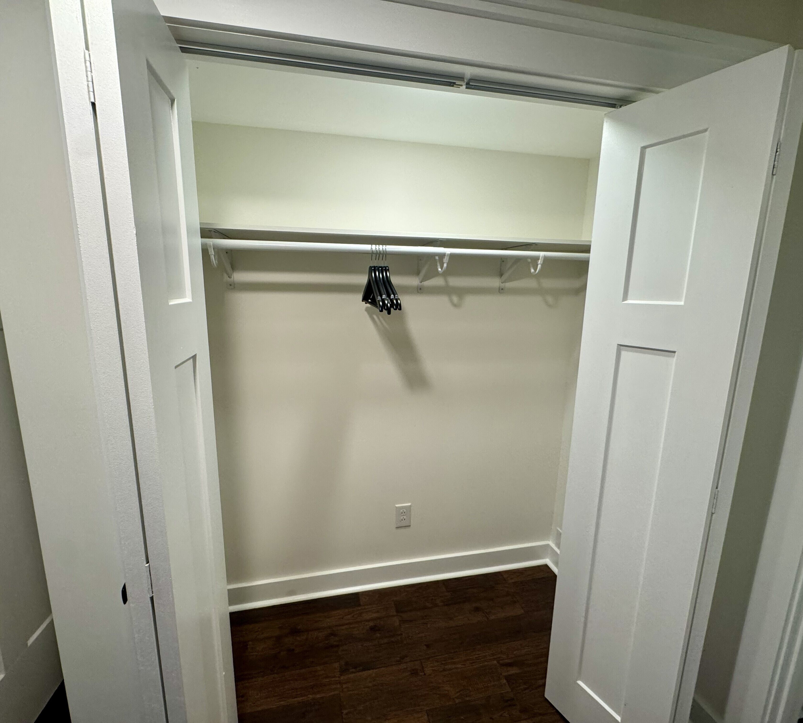 Un dressing accessible sans porte, doté d’un plancher en bois, d’une porte blanche et d’un porte-manteau avec des cintres.