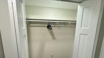 A walk-in closet with a wooden floor, a white door, and a coat rack with hangers.