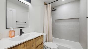 Un baño moderno con lavamanos blanco, tocador de madera, espejo, inodoro y zona de ducha.