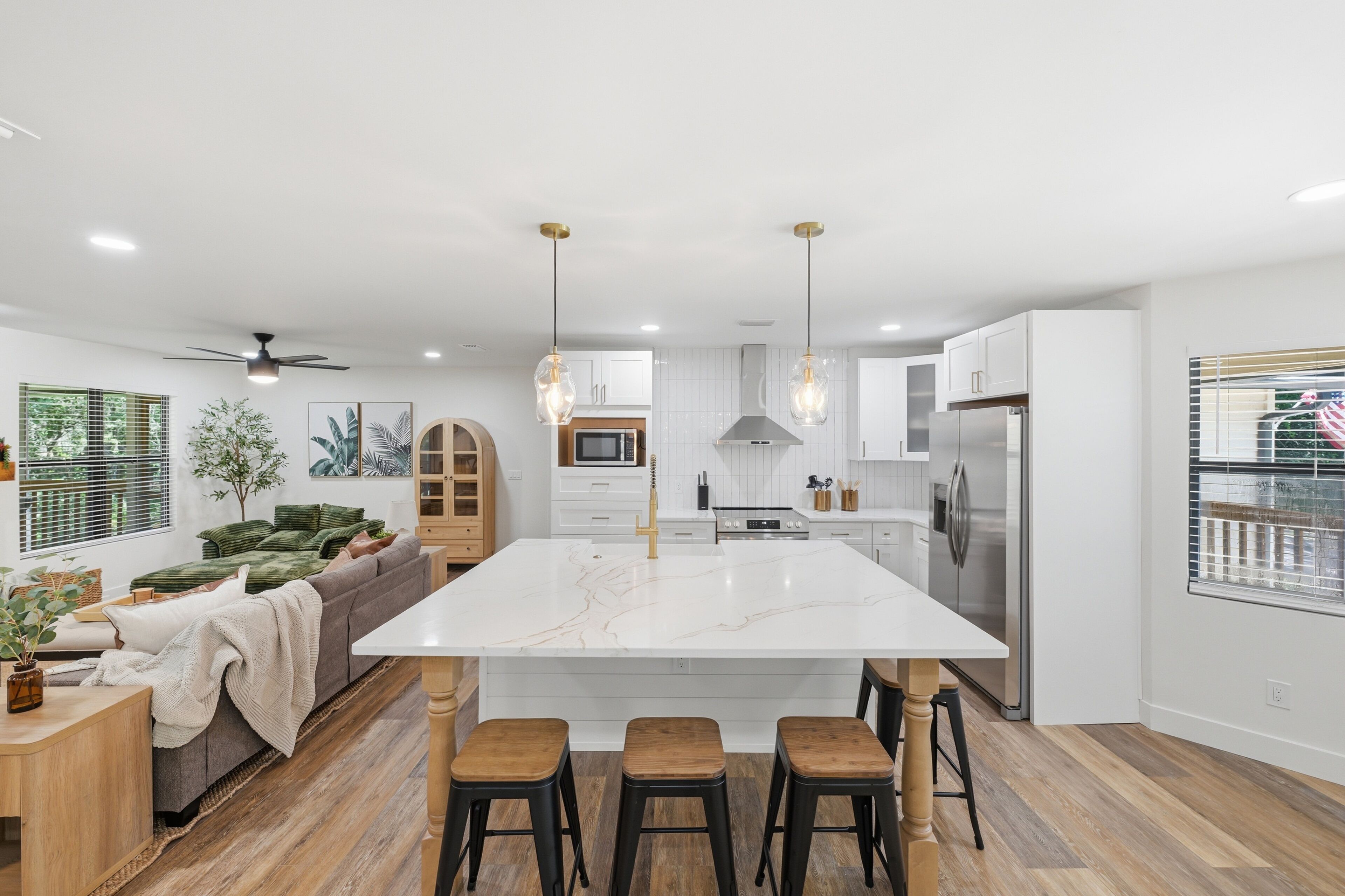 Une cuisine moderne avec un îlot central, des tabourets en bois et un ventilateur de plafond.