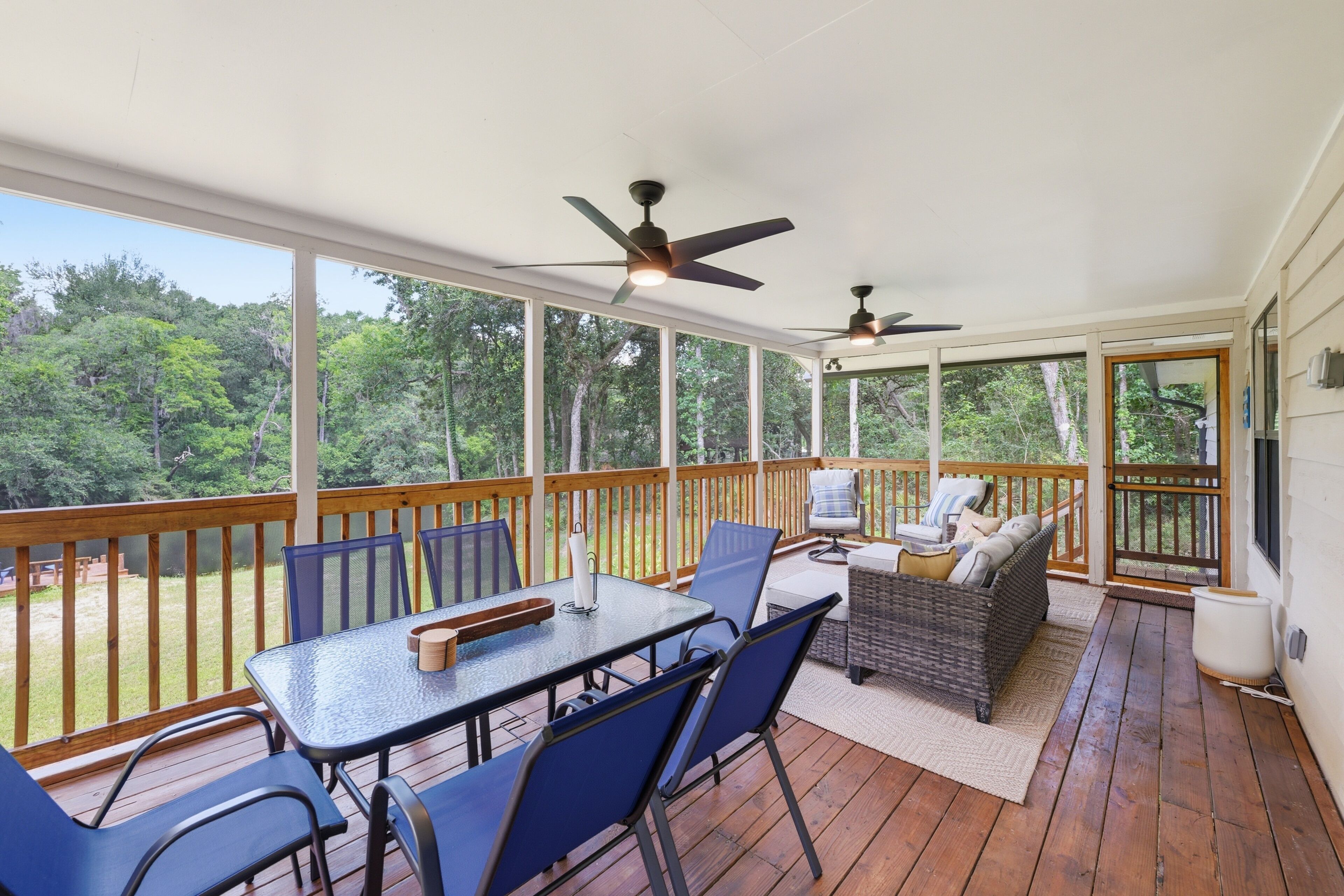 A covered outdoor deck with a table and chairs, a sofa, and two ceiling fans.