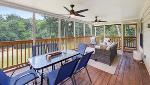 A covered outdoor deck with a table and chairs, a sofa, and two ceiling fans.