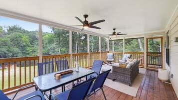A covered outdoor deck with a table and chairs, a sofa, and two ceiling fans.