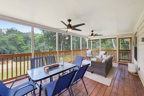 A covered outdoor deck with a table and chairs, a sofa, and two ceiling fans.