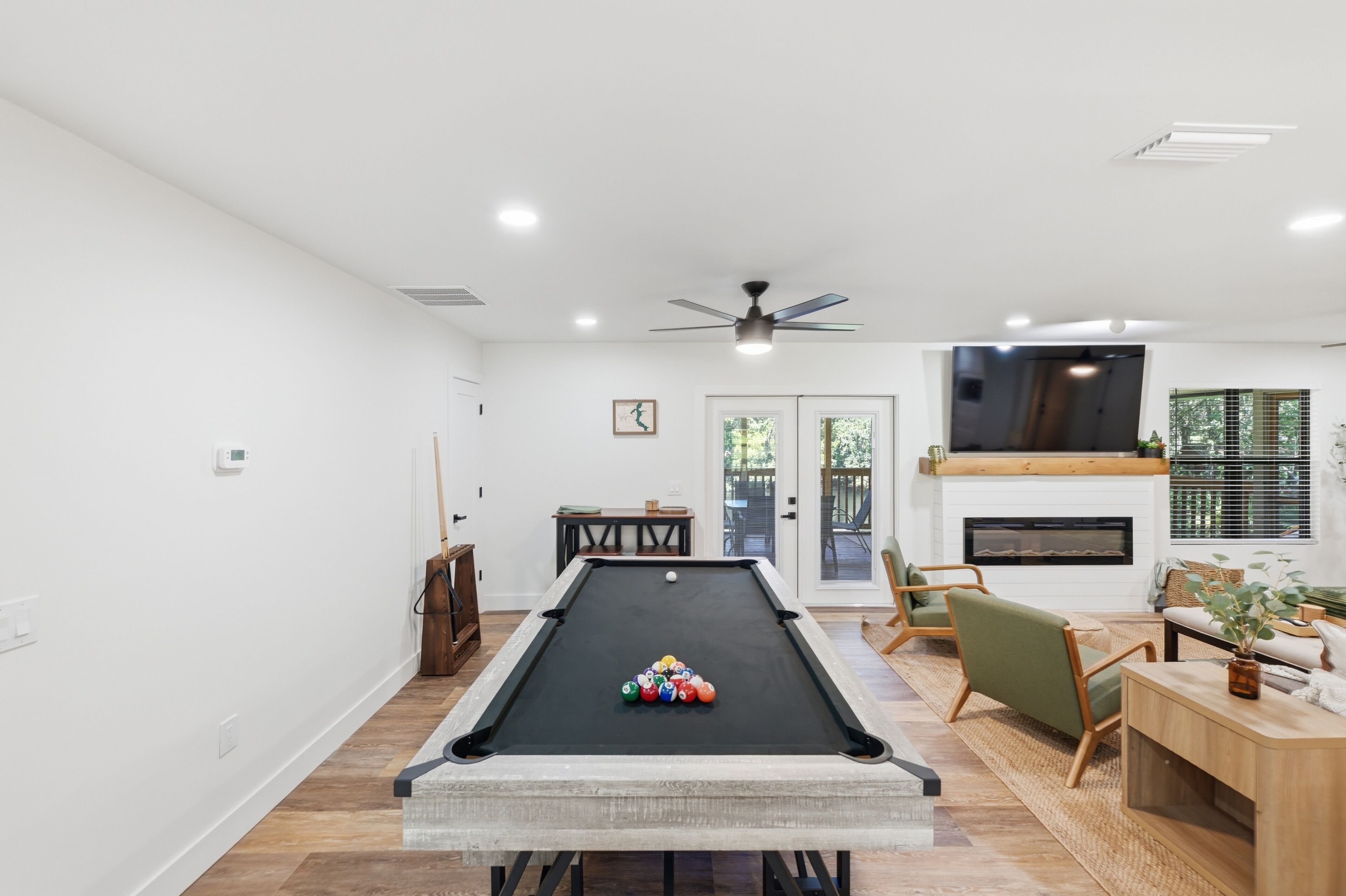 A pool table with balls, a ceiling fan, a fireplace, and a seating area with a TV.