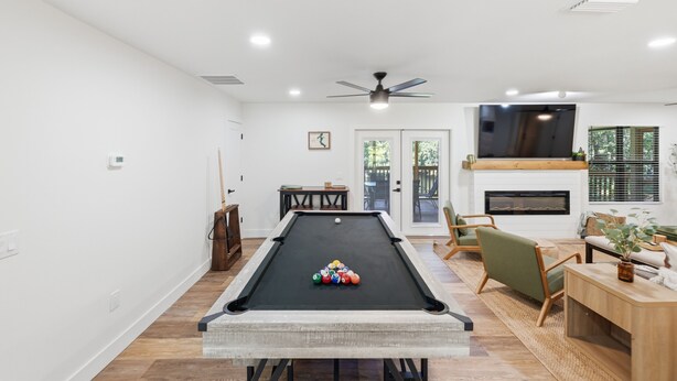A pool table with balls, a ceiling fan, a fireplace, and a seating area with a TV.