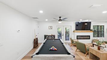 A pool table with balls, a ceiling fan, a fireplace, and a seating area with a TV.