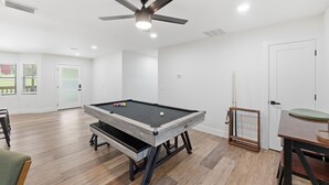 Una habitación amplia con mesa de billar, ventilador de techo y puerta que da a un balcón.