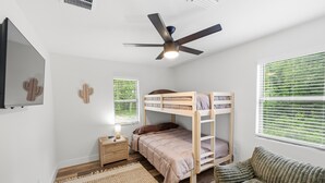 A bedroom with bunk beds, a ceiling fan, a bedside table with a lamp, and a window with blinds.