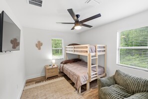 A bedroom with bunk beds, a ceiling fan, a bedside table with a lamp, and a window with blinds.