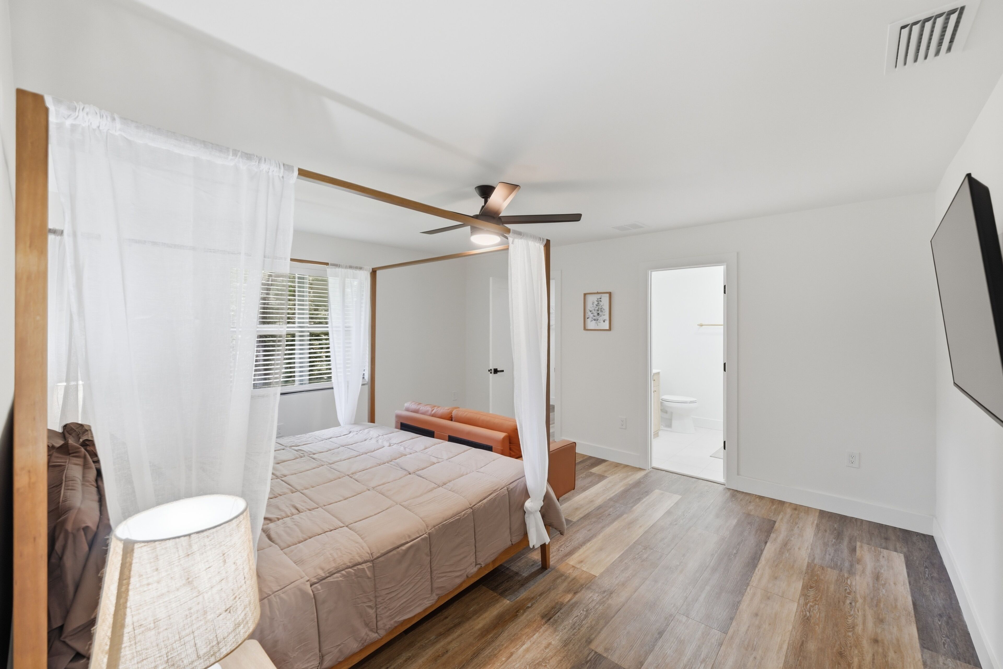 A bedroom with a four-poster bed, a ceiling fan, and a view of the bathroom.
