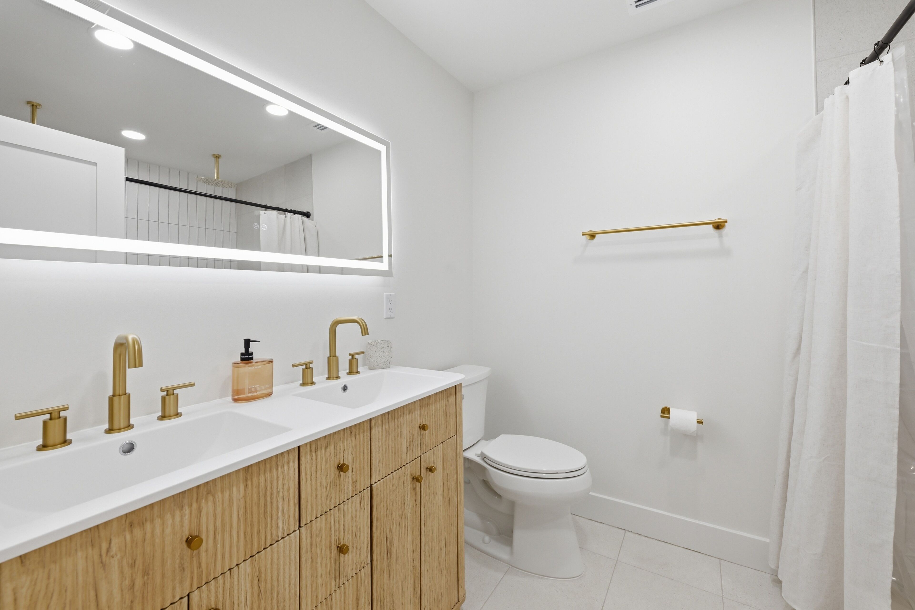A modern bathroom with a white vanity, gold fixtures, and a large mirror.