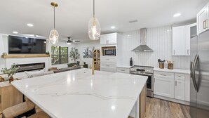Cocina moderna con armarios blancos, una isla grande, electrodomésticos de acero inoxidable e iluminación colgante.