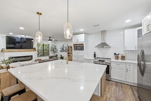 A modern kitchen with white cabinetry, a large island, stainless steel appliances, and pendant lighting.