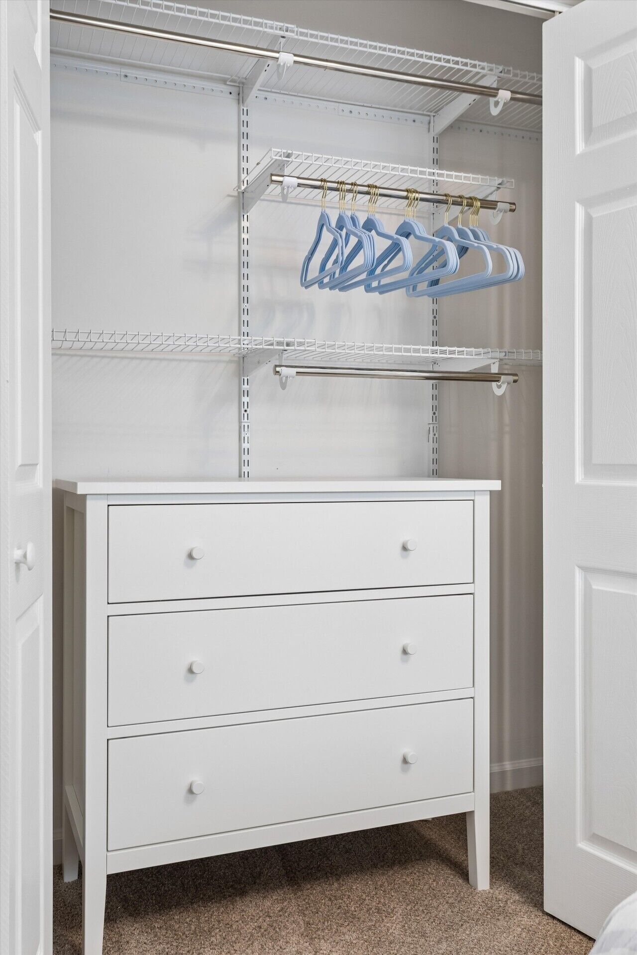 Une commode blanche à trois tiroirs, avec une étagère en métal au-dessus.