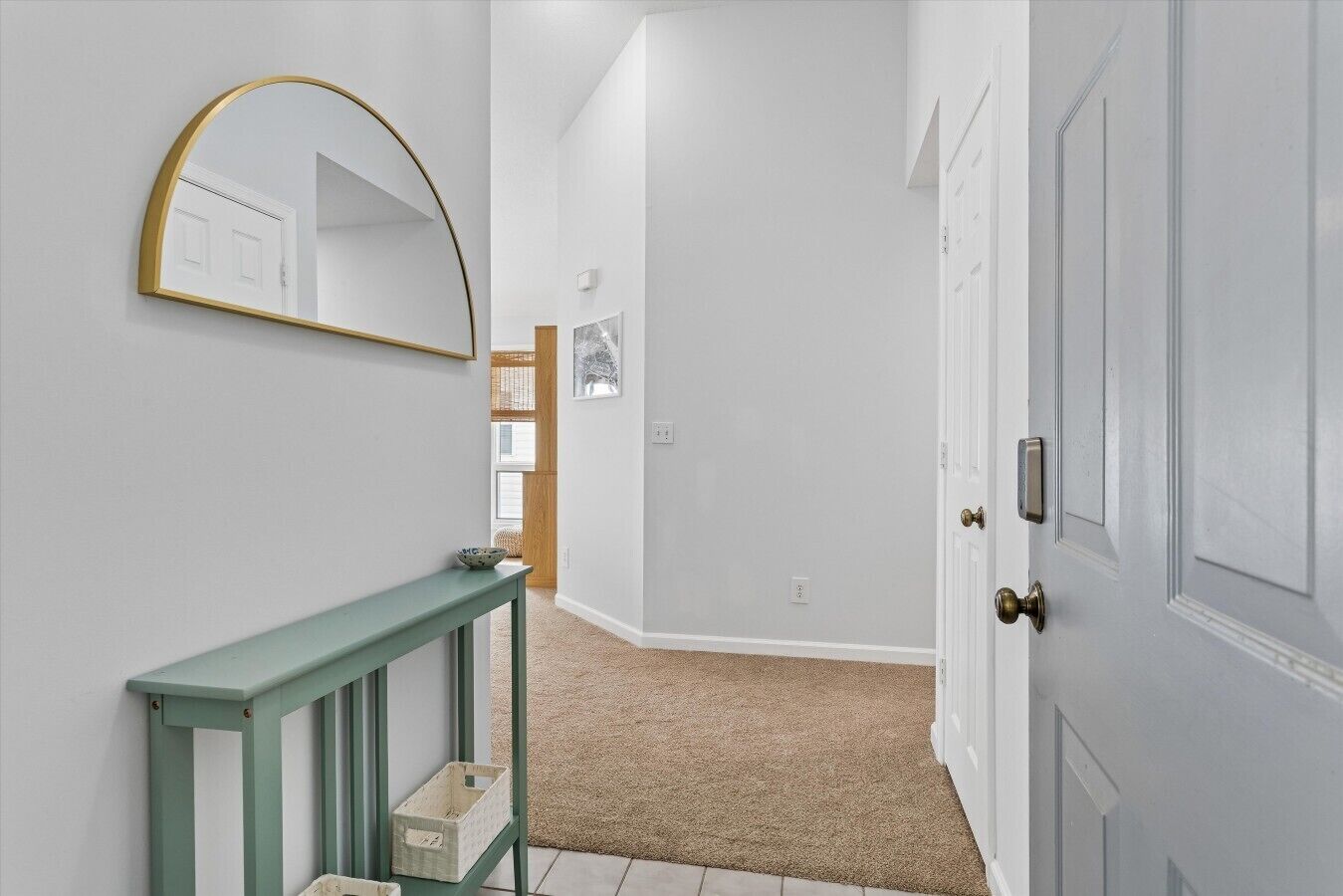 A hallway with a white door, a green console table, and a mirror on the wall.