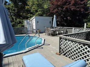 Eine Holzterrasse mit Pool, Liegestühlen und einem Tisch mit Stühlen.